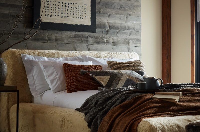 A hygge bedroom interior with faux fur bed frame, wood panelling, jute rug and neutral linen.