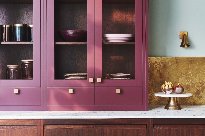 Plum painted cabinetry with wood base units and a metallic splashback.