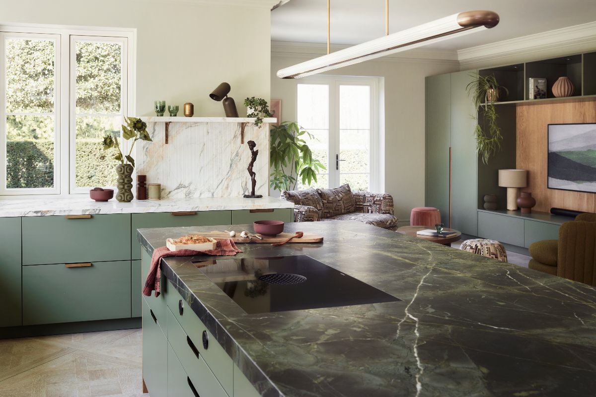 Green kitchen design with fluted marble, a central island topped with a rich stone worktop, open shelving, with an adjacent snug area.