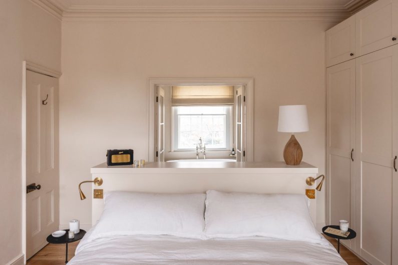 A small, white bedroom with built-in wardrobes, a central bed and an adjoining ensuite.