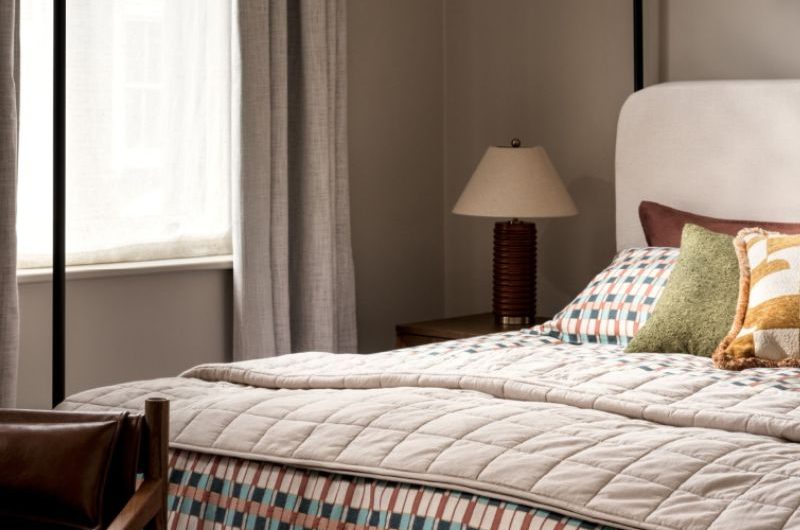 A chic boutique-hotel scheme with a poster bed, patterned linen, a leather chair and a wood bed with a reeded table lamp.