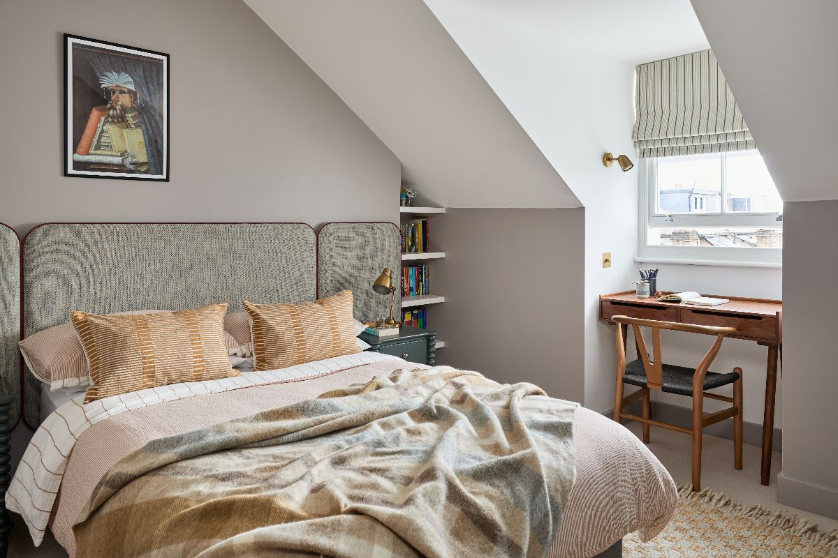A small, calm bedroom design with a desk by the window, built-in shelving and an upholstered bedframe.