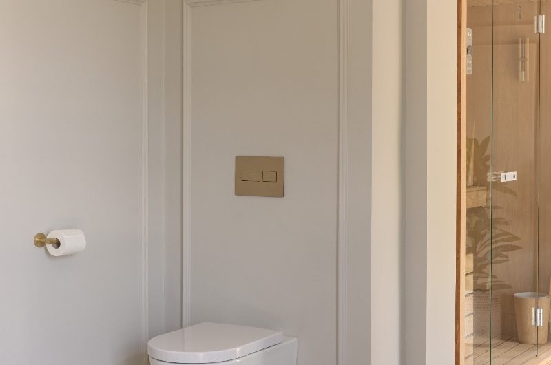 A minimalist design with wall panelling, a wall-mounted WC and gold flush plate and matching accessories.