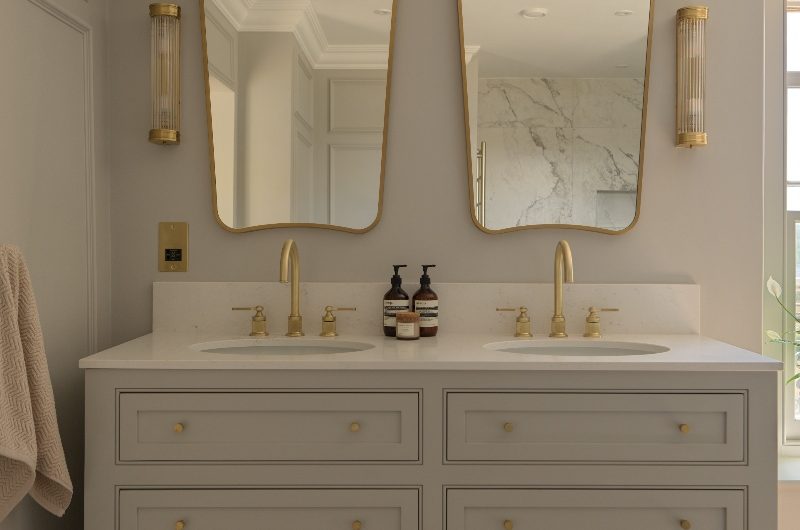A double vanity with inset basins, gold brassware, matching wall mirror and lights in a luxurious ensuite design.