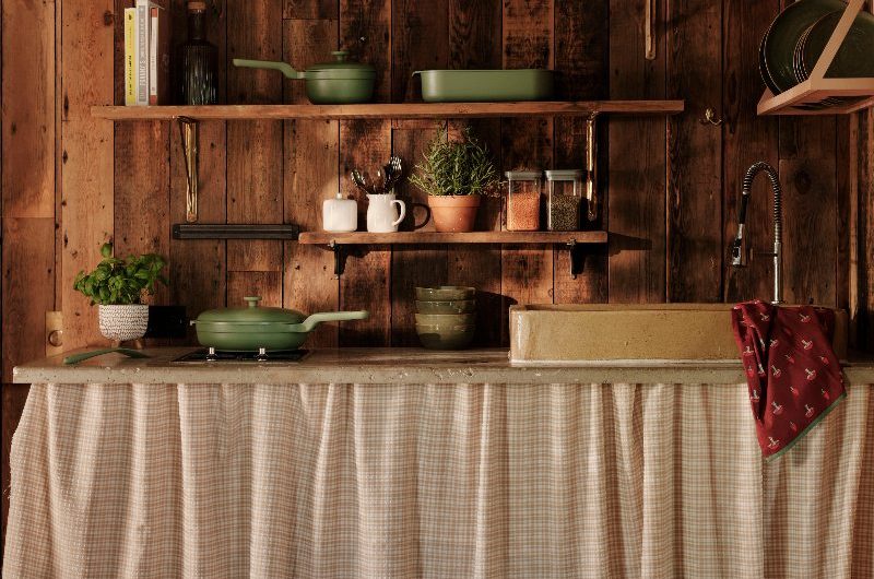 A sink zone in a country-style scheme with open shelving, a stone work surface and gingham curtain.