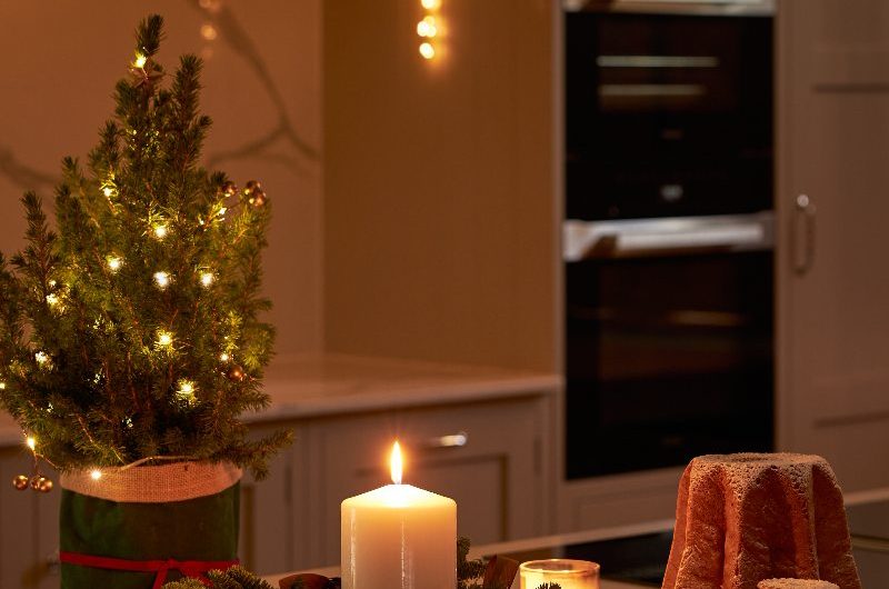 A Shaker kitchen design with Christmas decorations such as a small tree, wreath with candle, and mince pies, on the island.