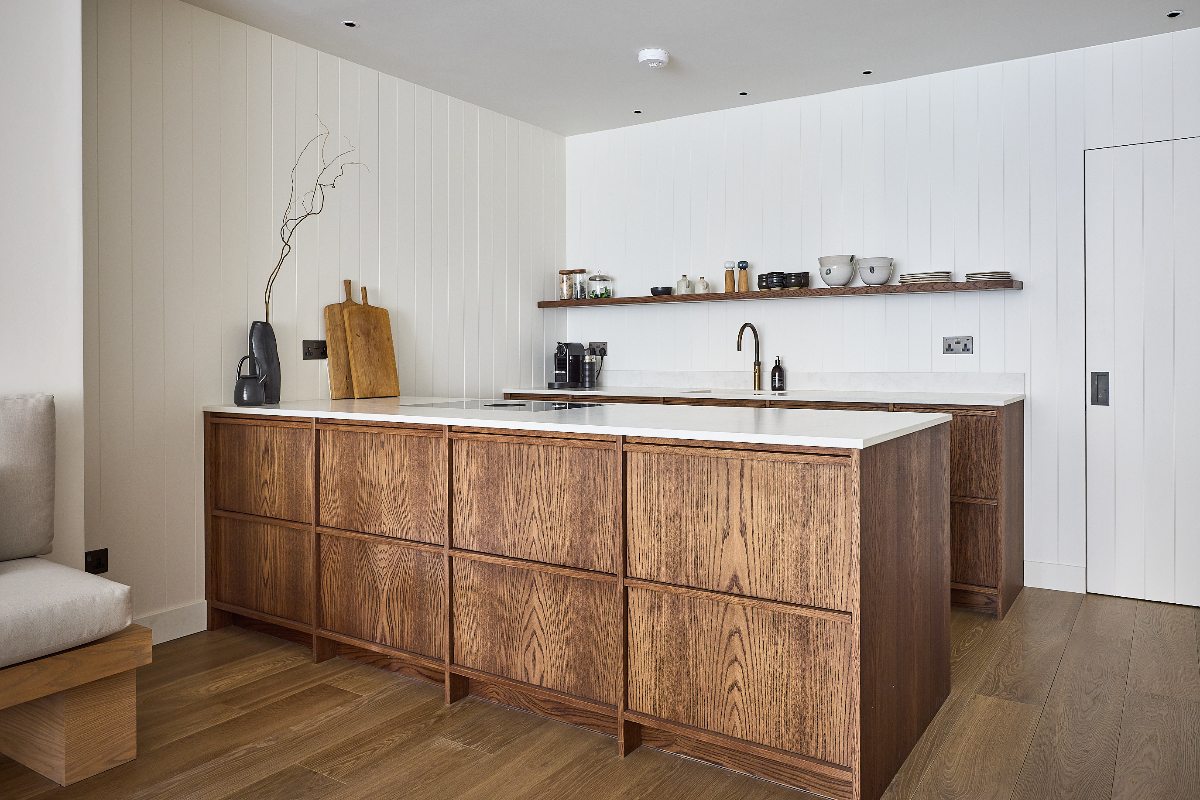 Kitchen design with wood base units and a matching peninsula, wood panelling on the walls painted in white, wood flooring and white worktops.