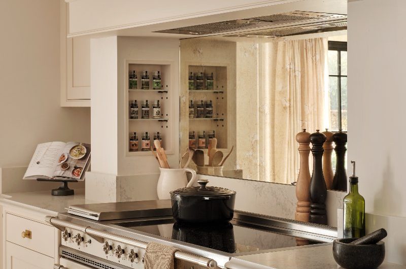 A country-style kitchen with Shaker cabinets, a cream coloured range cooker with induction hob, a concealed extractor, and mirrored splashback.