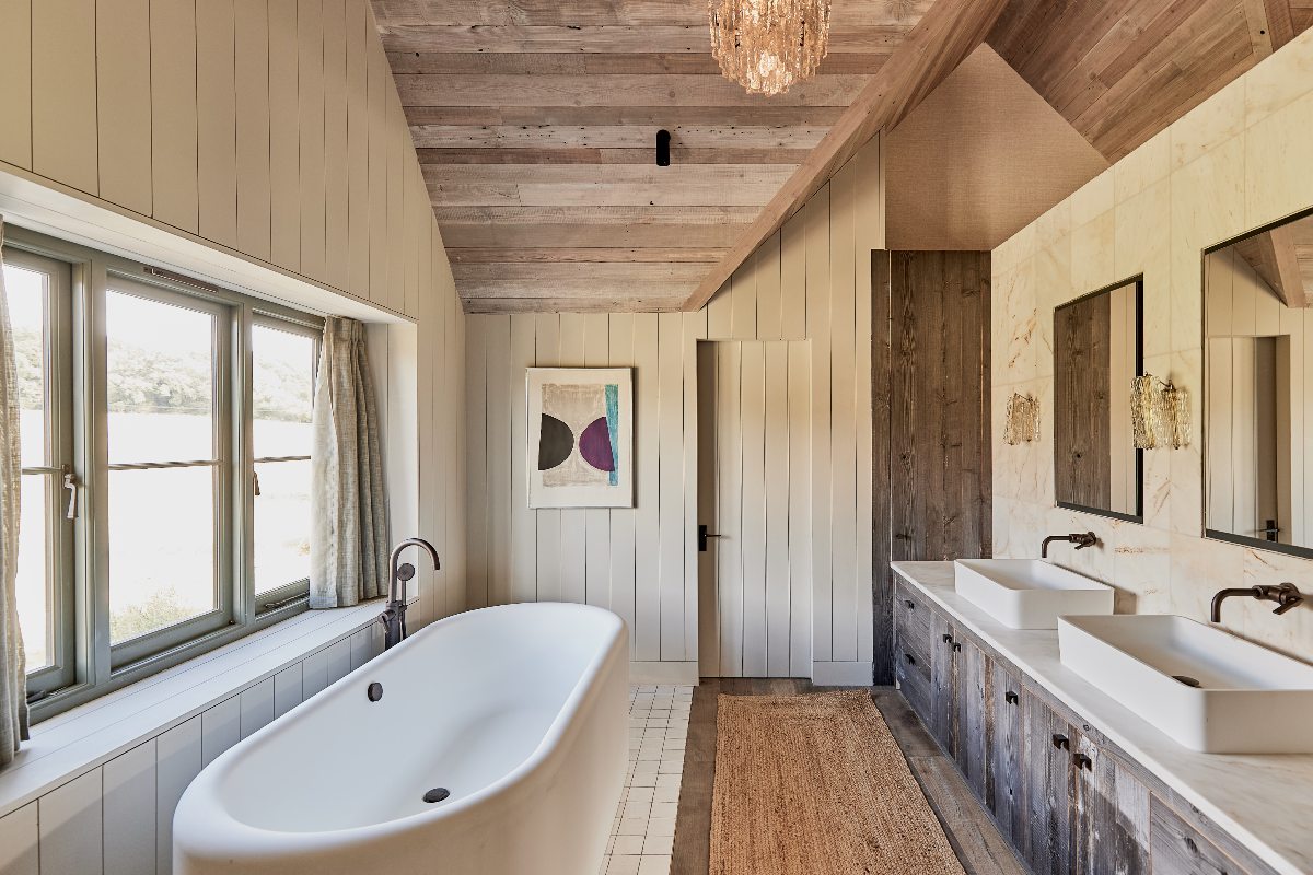 Rustic bathroom with reclaimed surfaces on the ceiling and floor, white and marble-effect tiles, a double basin and vanity zone, and a freestanding tub.