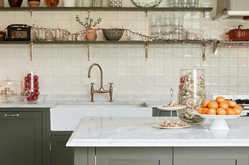 A charming green kitchen design with white zellige tiles, green base units, and a freestanding island with Christmas decorations.