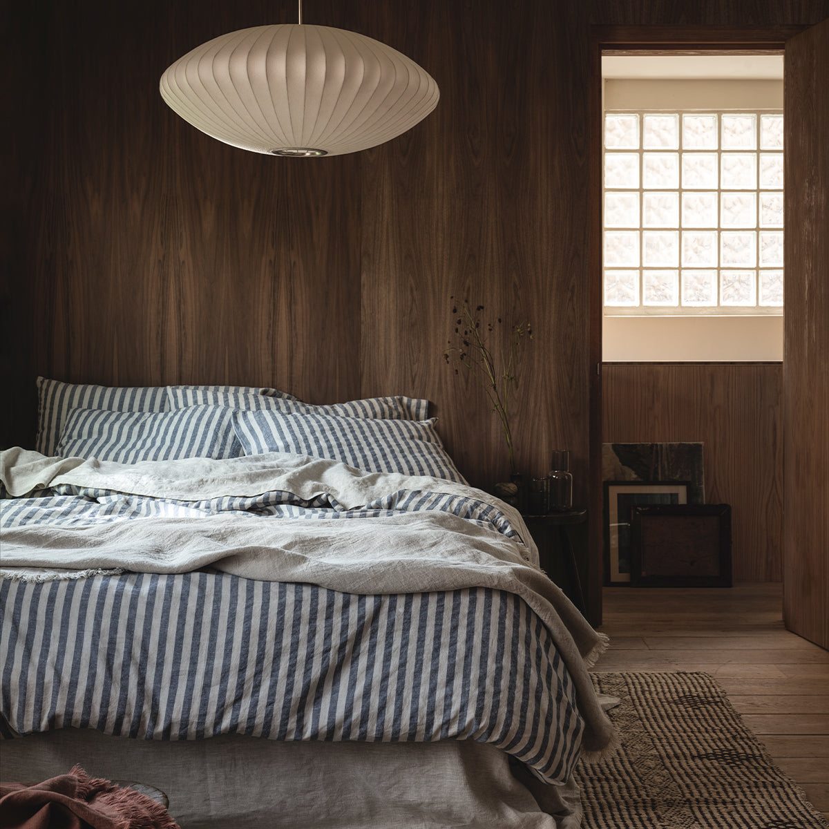 Wood drenched bedroom with a central bed dressed in striped linen, with a textured rug underneath.