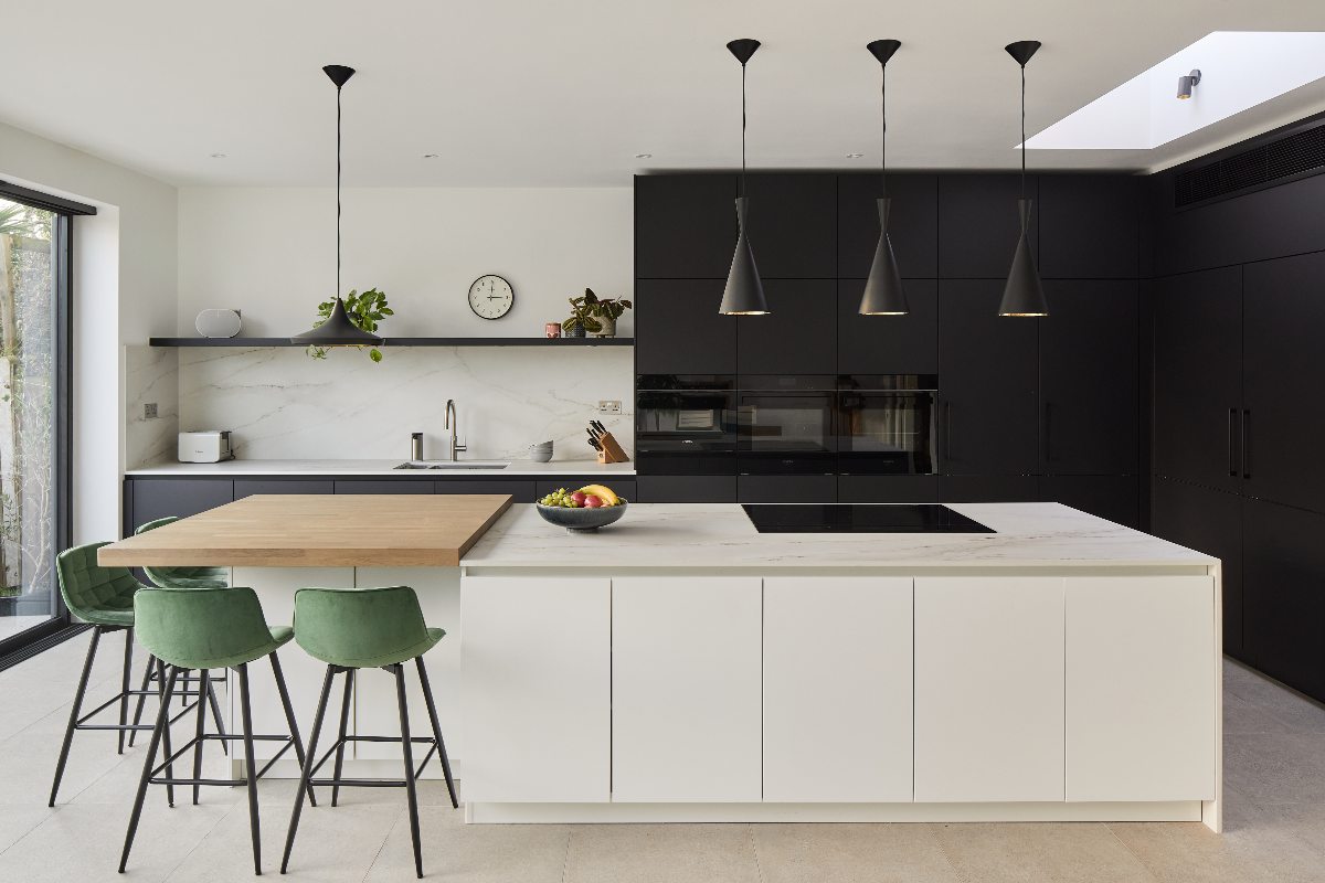 L-shaped floor to ceiling cabinetry with matt black handles, a central island with seating and dining space, and neutral surfaces.