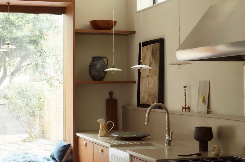 A fusion style kitchen with statement stainless steel appliances, wood cabinetry, concrete-effect surfaces, and a reading nook by the window.