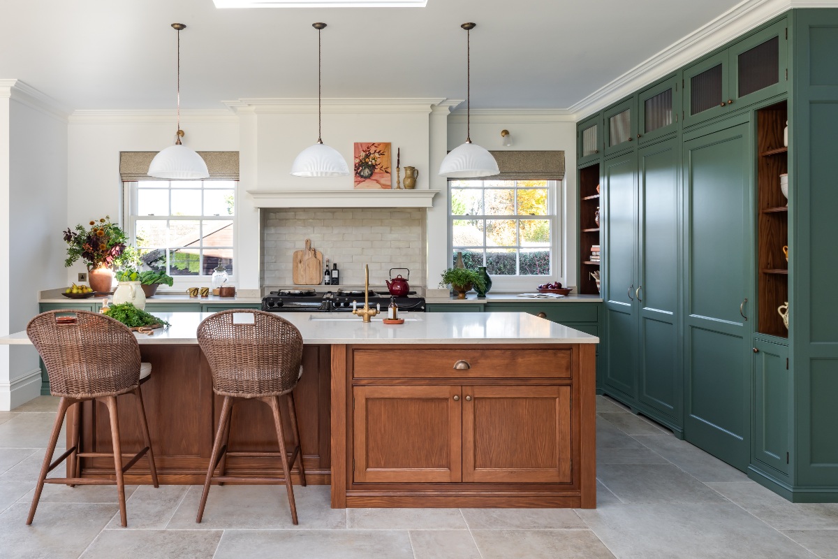An L-shaped kitchen painted in a vivid green colour, with a smoked oak island with seating and white surfaces.