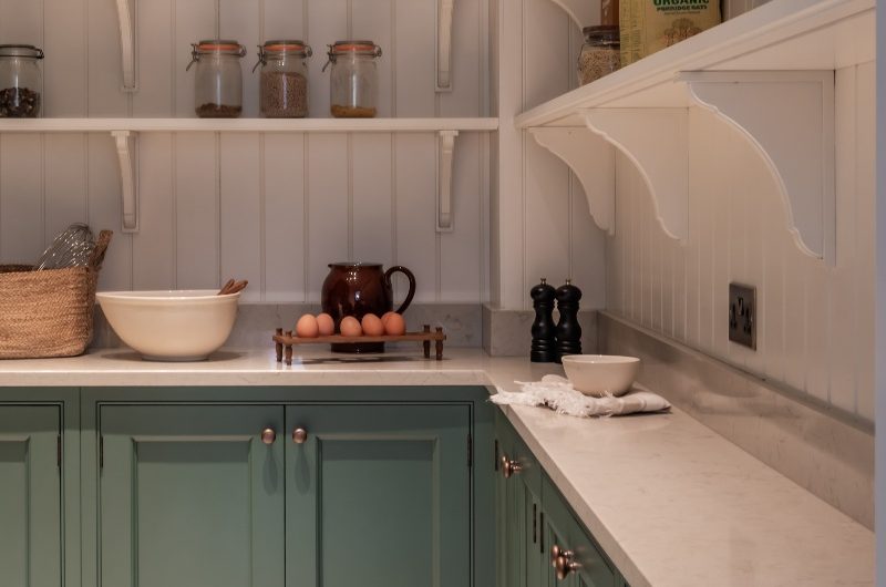 A walk-in pantry with classic cabinetry, open shelving, wall panelling, and stone worktops and splashbacks.