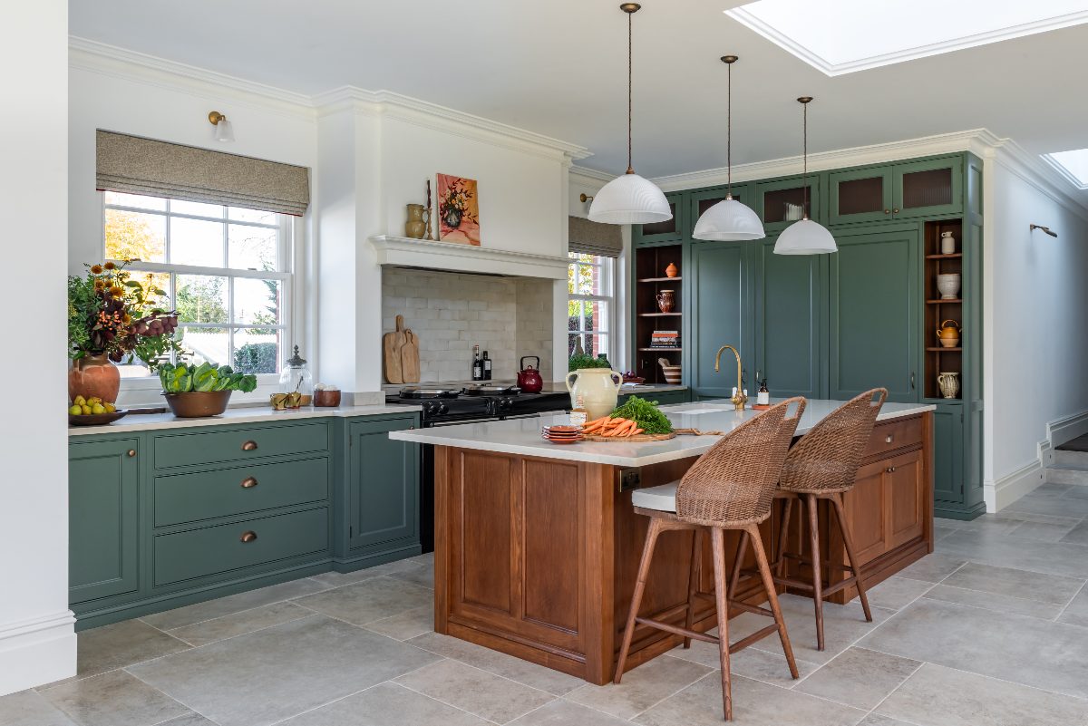 A charming classic kitchen with green base units, a smoked oak island, a range cooker in an alcove with a concealed extractor, and neutral worktop and flooring surfaces.