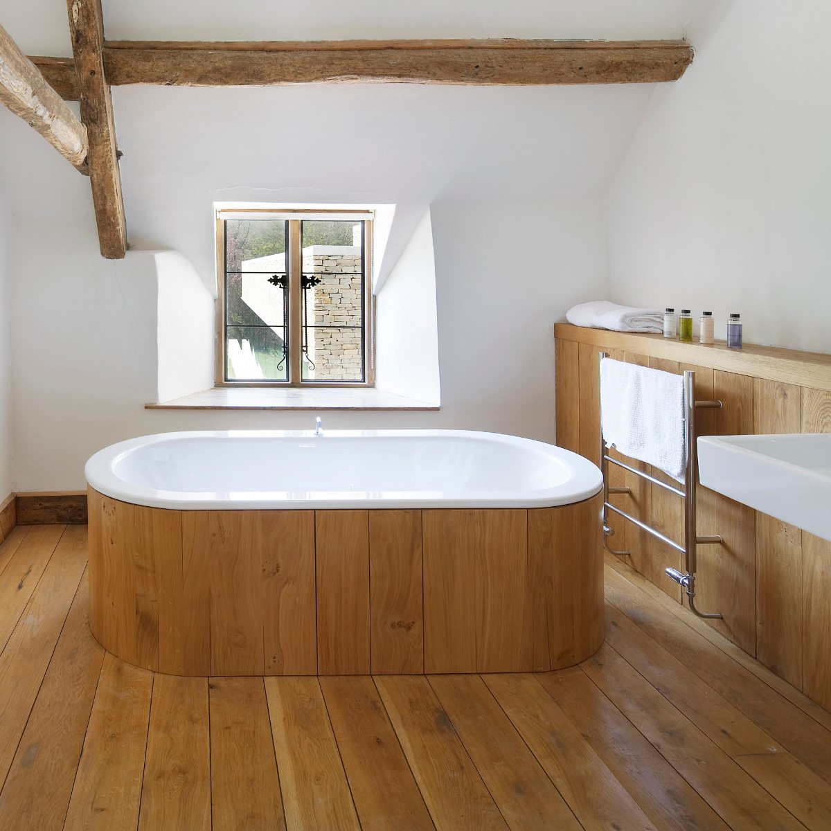 Classic bathroom design with a sloped ceiling, wood panelling, flooring and a panelled tub, with chrome brassware and radiator and white sanitaryware.