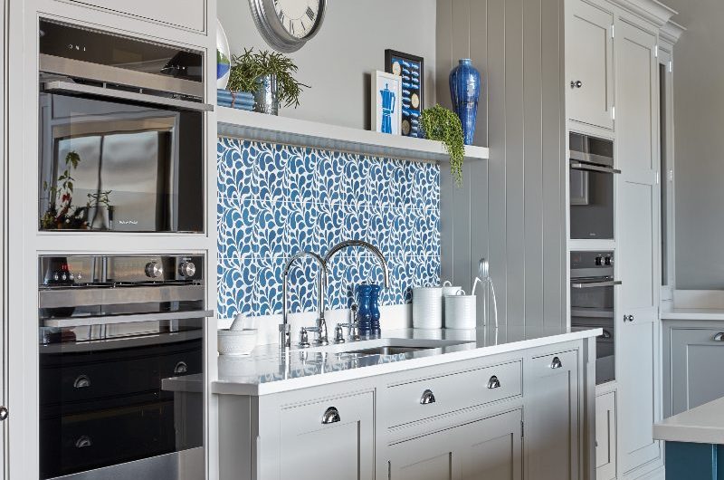 A classic scheme with grey cabinetry, patterned tiles, exposed wooden beams and integrated cooking gadgets.