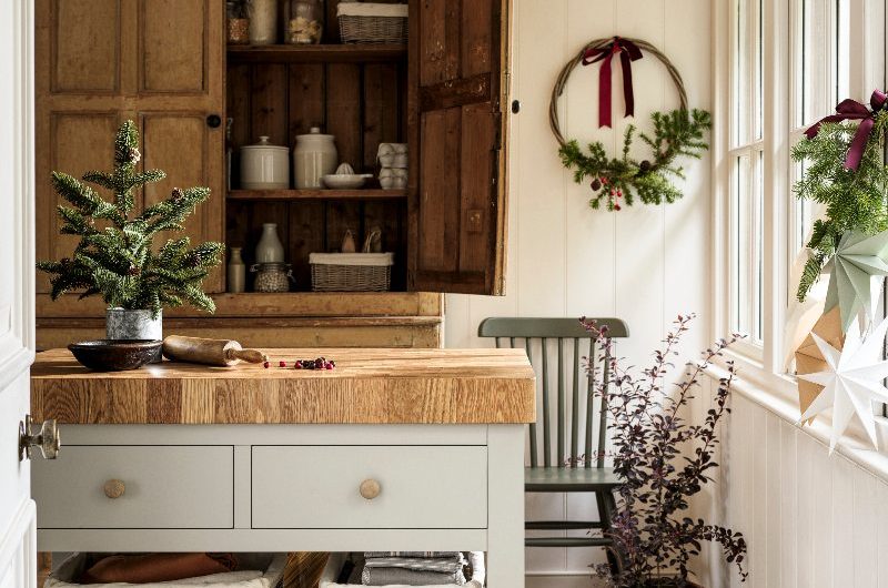 Country chic kitchen with wall panelling, a wood freestanding dresser, a freestanding island, festive decor, and stone flooring.