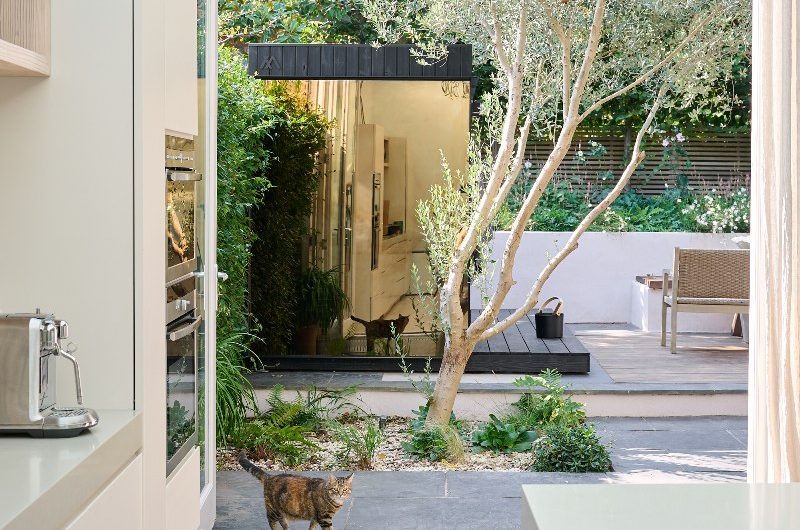 A neutral kitchen design looking out onto the garden which has a sauna with a customised privacy glass.