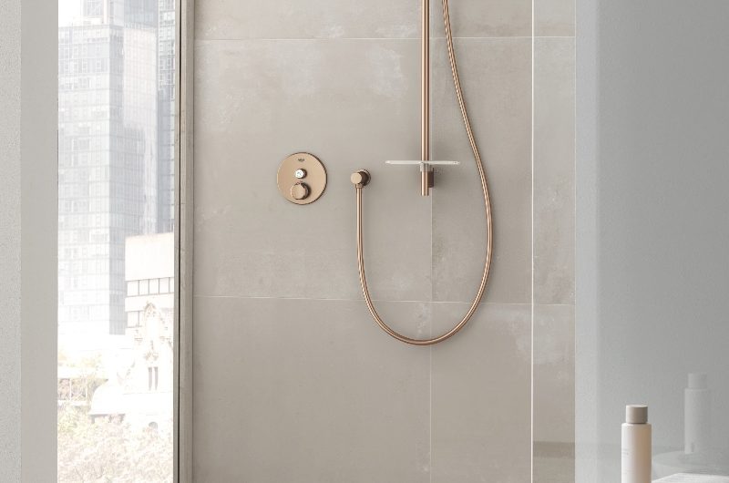 A neutral, calm wetroom with large-format wall and floor tiles, copper shower system and a tall window.