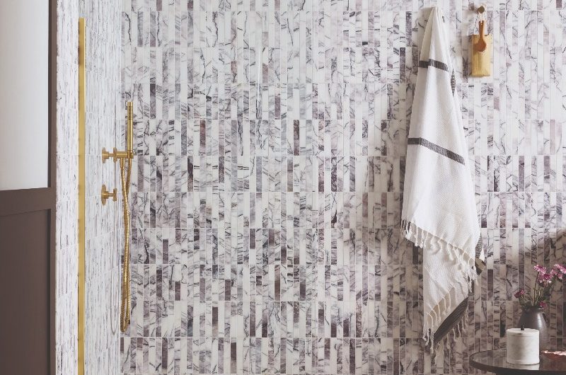 A shower zone drenched in micro marble kit-kat tiles, large-format tile flooring, a gold enclosure and a matching gold shower system.