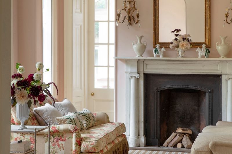 Regencycore style living room with a floral sofa, striped carpet, elegant lighting and a fireplace.