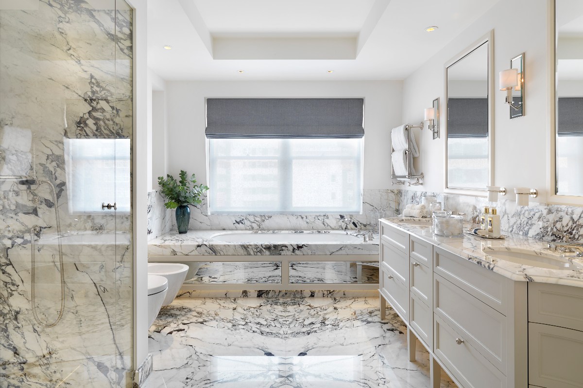 A bathroom drenched in marble surfaces, with a fitted tub, shower zone, and a grand double vanity unit.