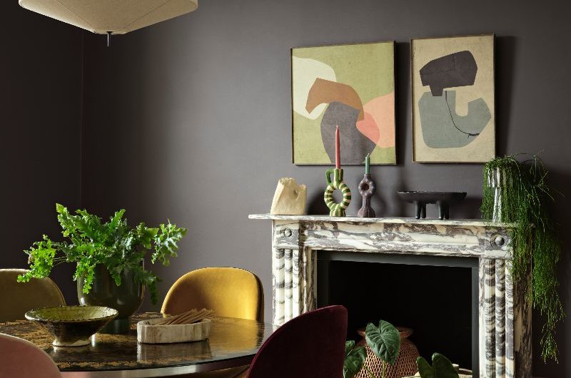 A dark and moody living room with a marble fireplace, wood flooring, a metallic table and velvet chairs.