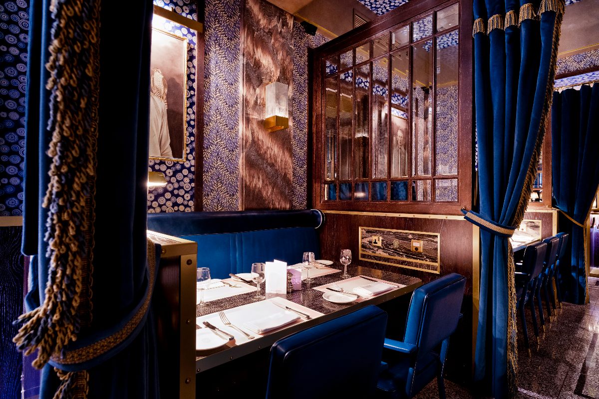 Bob Bob Ricard London's opulent restaurant interiors with moody wallpaper, royal blue booths and chairs, dark wood furniture and chunky velvet curtains.