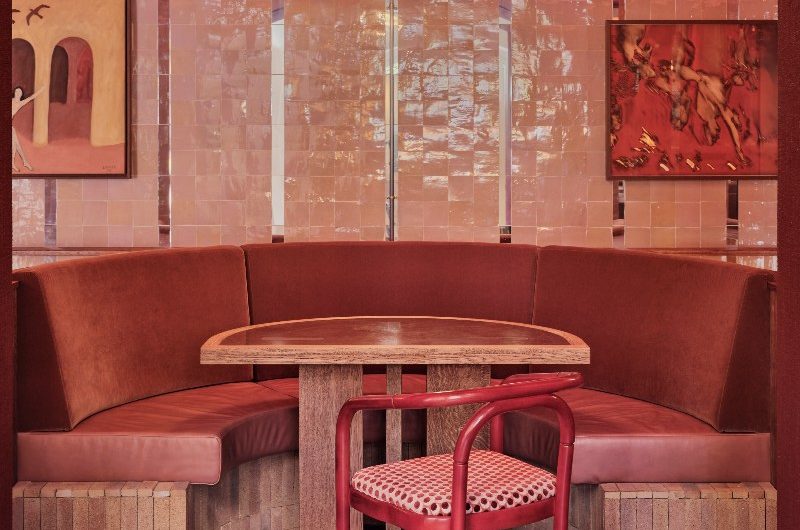 A modern restaurant with pink zellige tiles on the walls, a curved banquette and checkered wood floors.