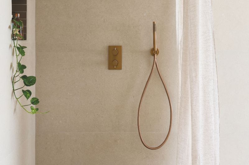 A calm, off-white shower design with large-format tiles, bronze brassware and an airy curtain.