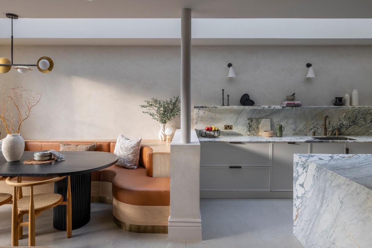 A modern kitchen with slim Shaker cabinets, marble surfaces and a dining zone with a leather banquette.