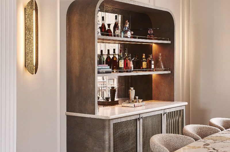 A dining room with wall panelling, wall lighting, a marbled table, contemporary chairs, and a curved home bar with open shelving and mesh door frames.