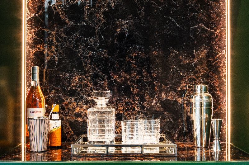 Closeup at a drinks area with dark green fluted furniture, dark stone, and LED lighting.