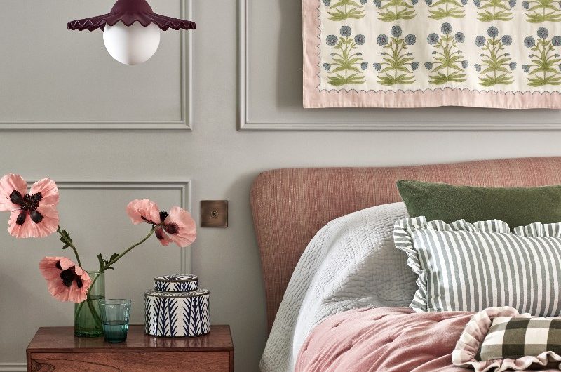 A calm bedroom design with wall panelling, a pink frame with a mix of soft furnishings and a wood bedside table.