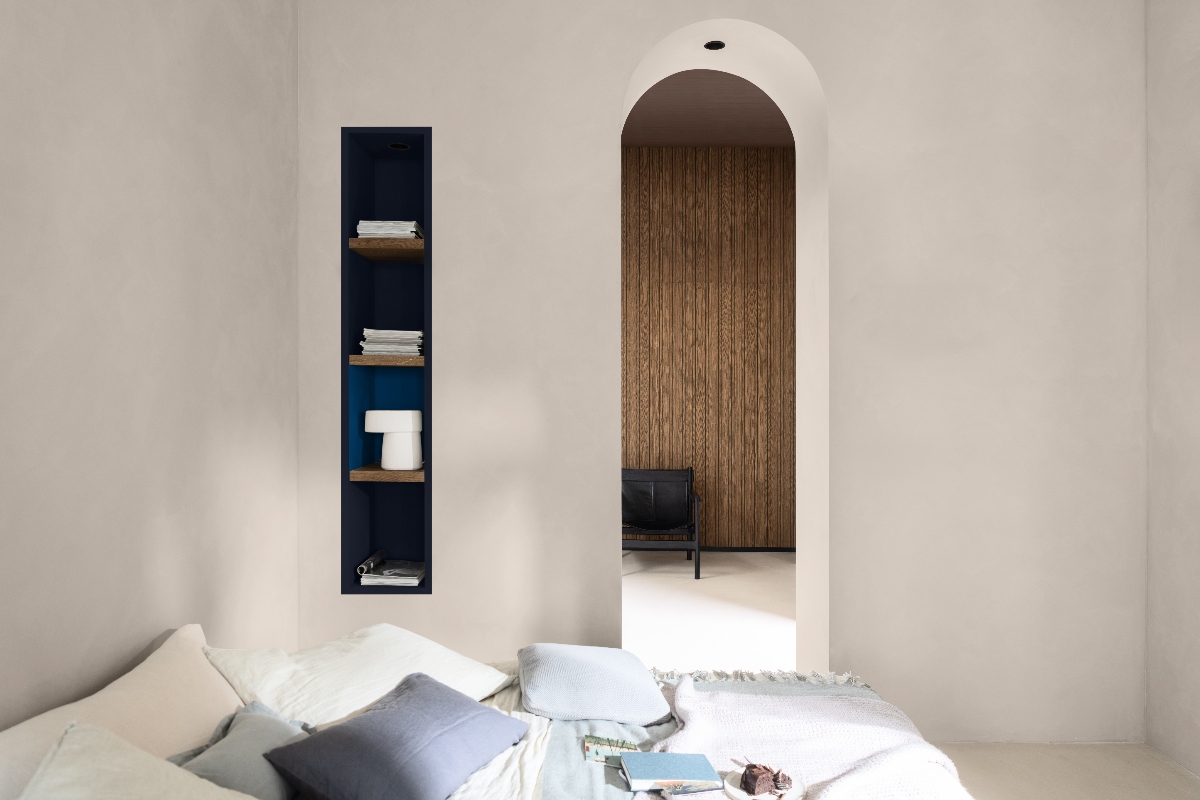 A neutral bedroom with an arched entryway, open shelves, and a bed frame with pastel linen.