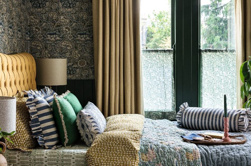 A statement bedroom design drenched in patterns with a mustard yellow bed frame, striped and floral soft furnishings and patterned cafe curtains on the window.