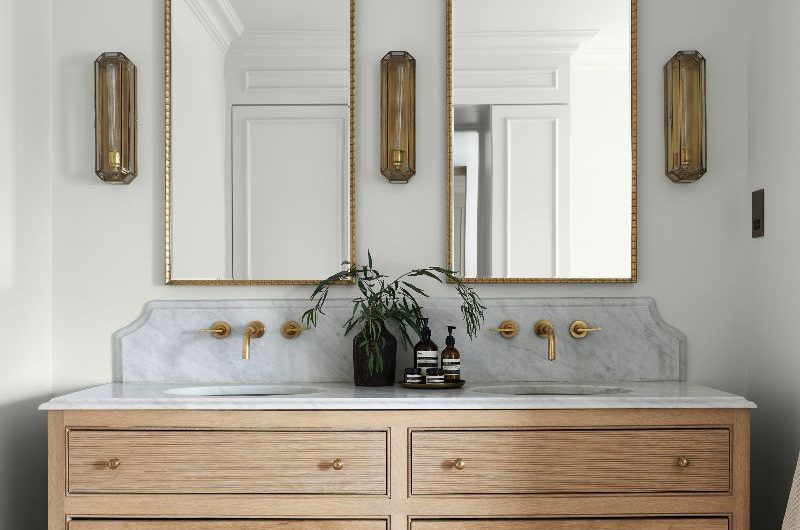 A chic, rustic bathroom with a double vanity unit, terracotta flooring, and brass finishes.
