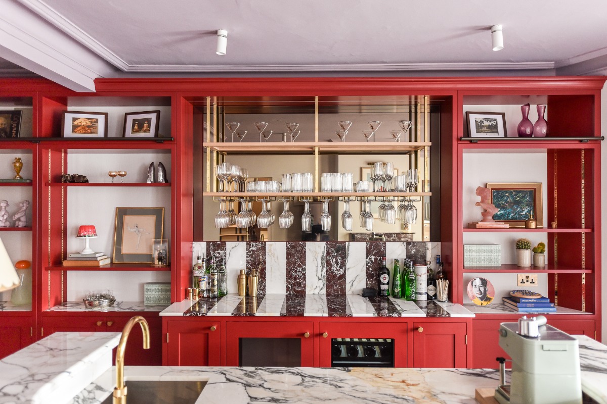 A colourful home bar with red furniture, a mix of marble surfaces, built-in appliances, and mirrored splashback.