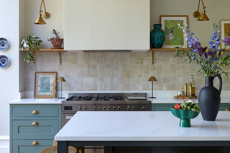 A cooking run with a range cooker, green base units, zellige tiles, a concealed extractor, open shelving, and a dark green island with white worktops and wood bar stools.