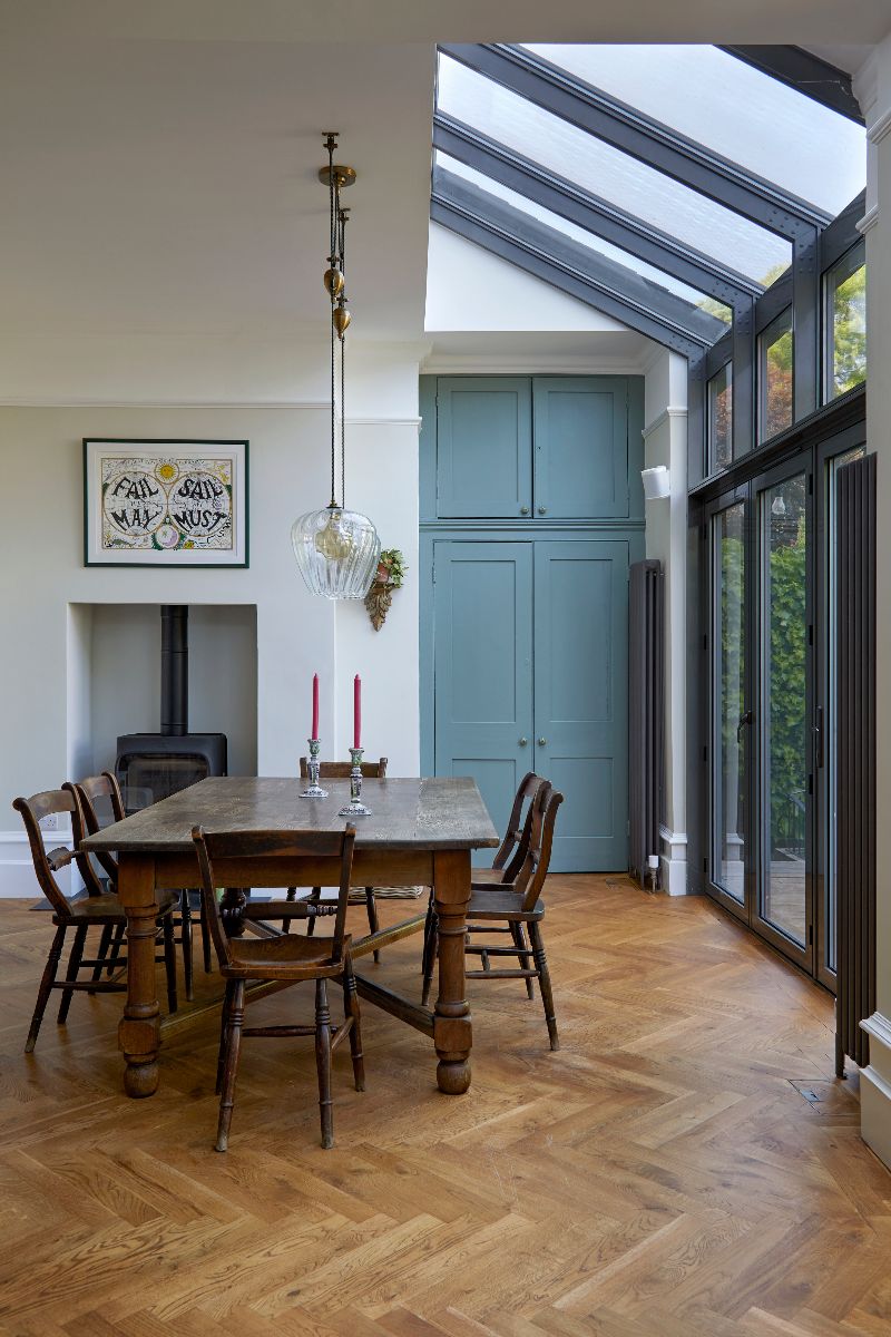 A dining area with parquet flooring, vintage table and chairs, a wood burner, and glazing.