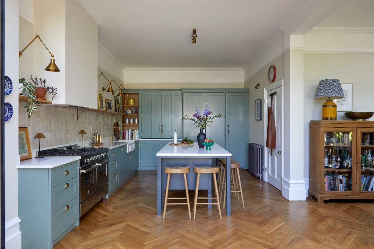 A warm and welcoming kitchen design in an L-shaped layout with a central island, painted in green, with parquet flooring.