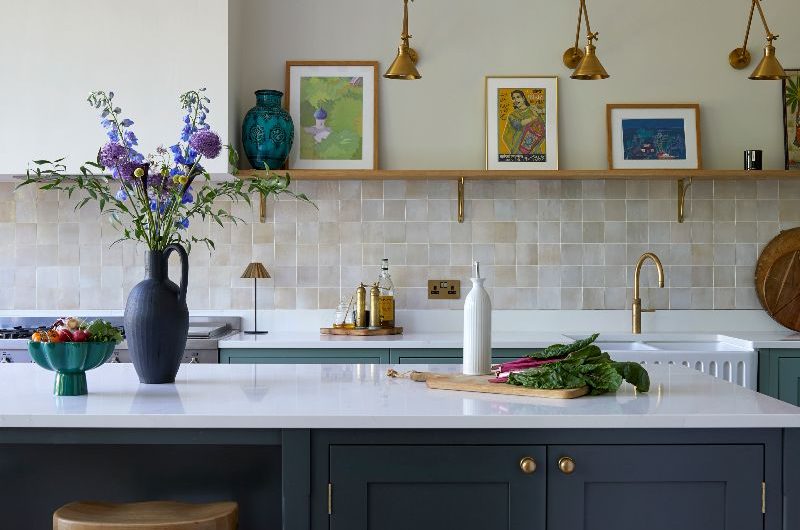 A warm kitchen design with pinky glazed zellige wall tiles, white countertops, light green base units, a dark green island, and neutral paint colour on the walls.