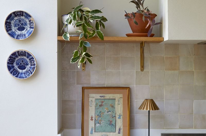 Closeup at the kitchen run with white worktops, pinky zellige tiles, open shelf with plants on display, and green base units.