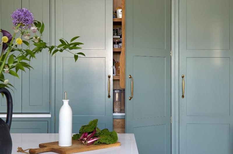 A tall run of cabinets with a pantry and deep drawers, painted in a calm green.