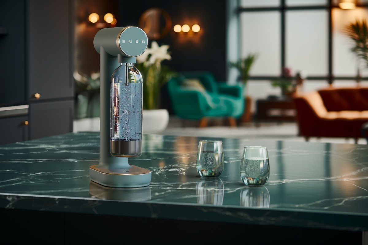A soft green soda machine on a green marble countertop.