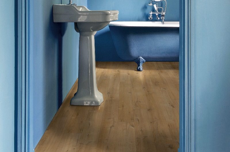 A Regencycore bathroom drenched in blue with a classic bath, white pedestal basin, and wallart.