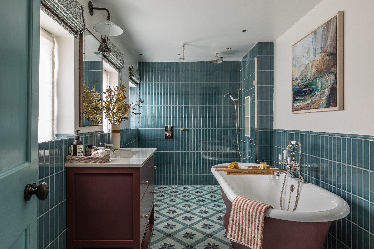 A blue bathroom design with metro wall tiles, patterned flooring, a burgundy vanity and matching painted tub.