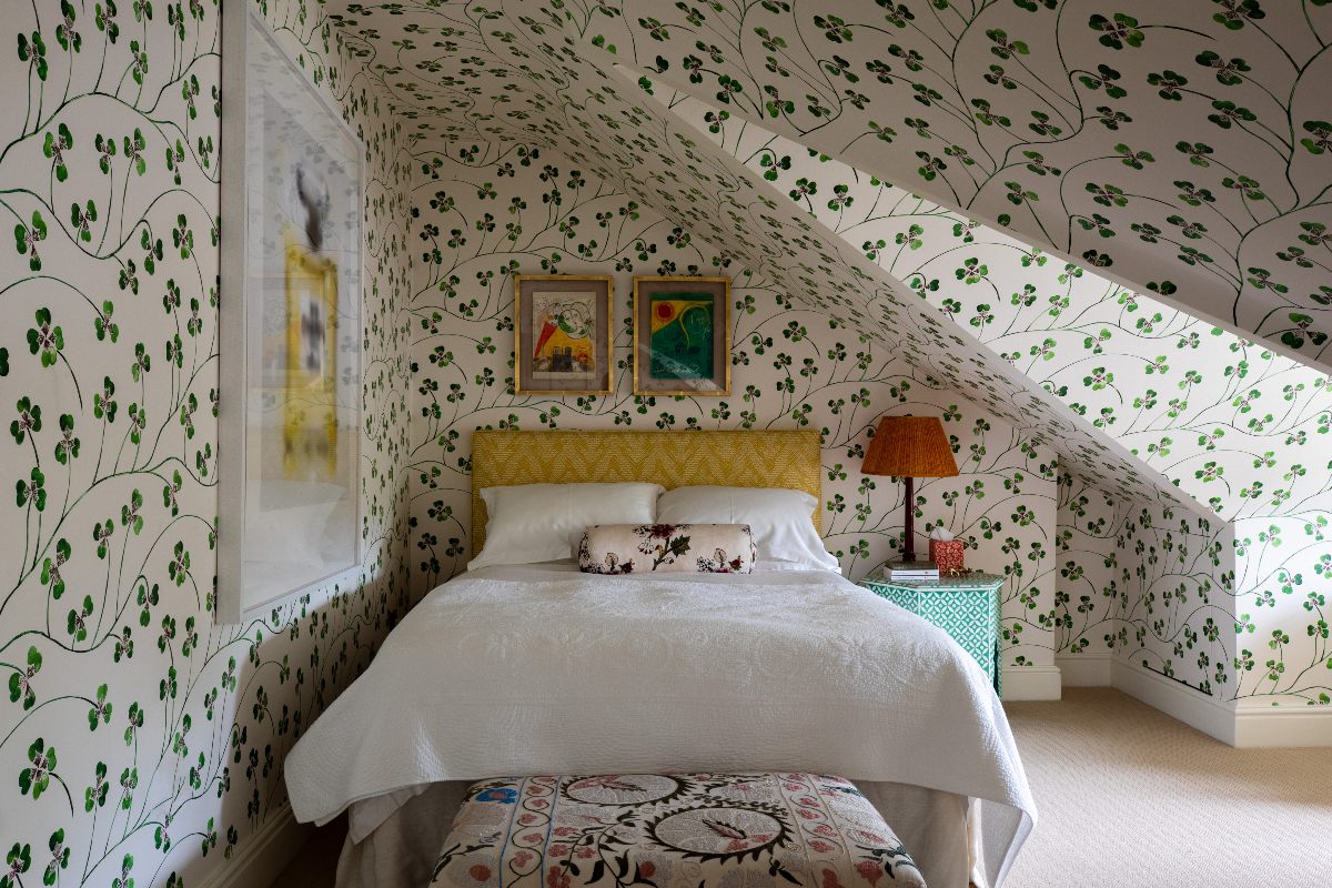 A loft bedroom with clove leaf wallpaper on the walls, a yellow bed frame, wall art, and colourful decor.